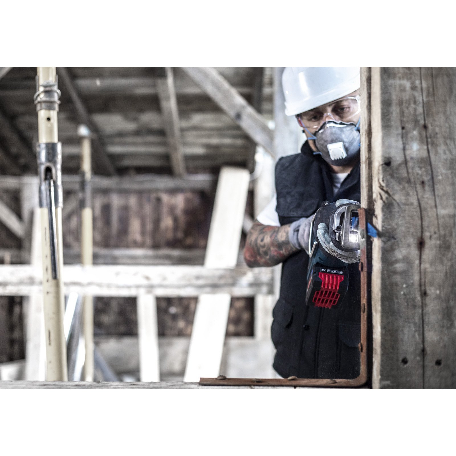 Robotnik w masce oddechowej i kasku używa piły do cięcia drewnianej konstrukcji. Jest na budowie.