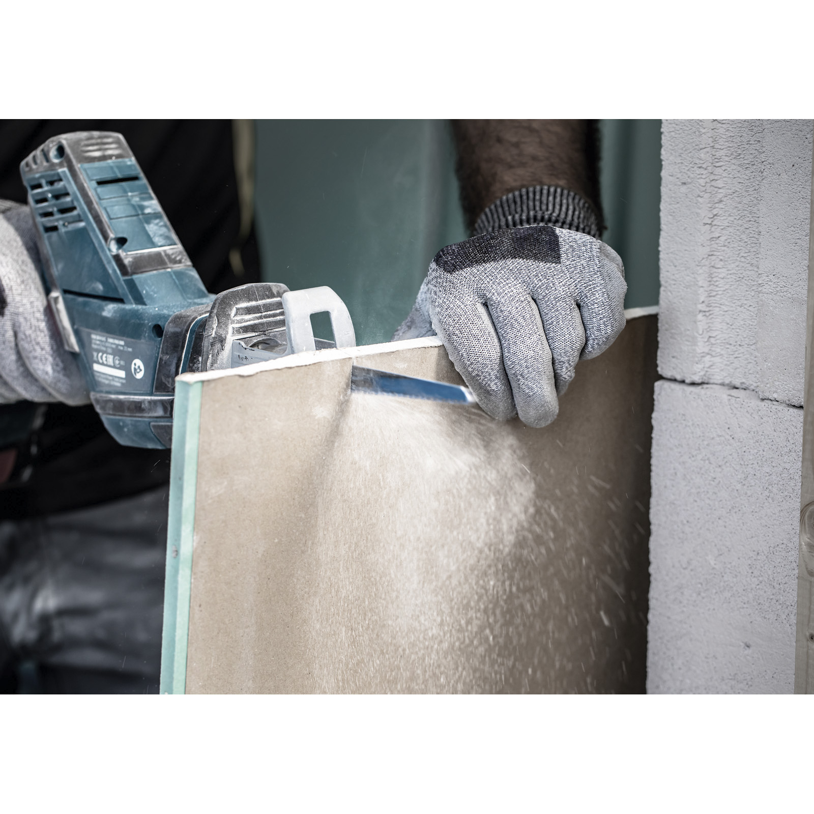 Osoba używa piły do cięcia płyty gipsowo-kartonowej. Piła jest trzymana przez dłoń w rękawicy.