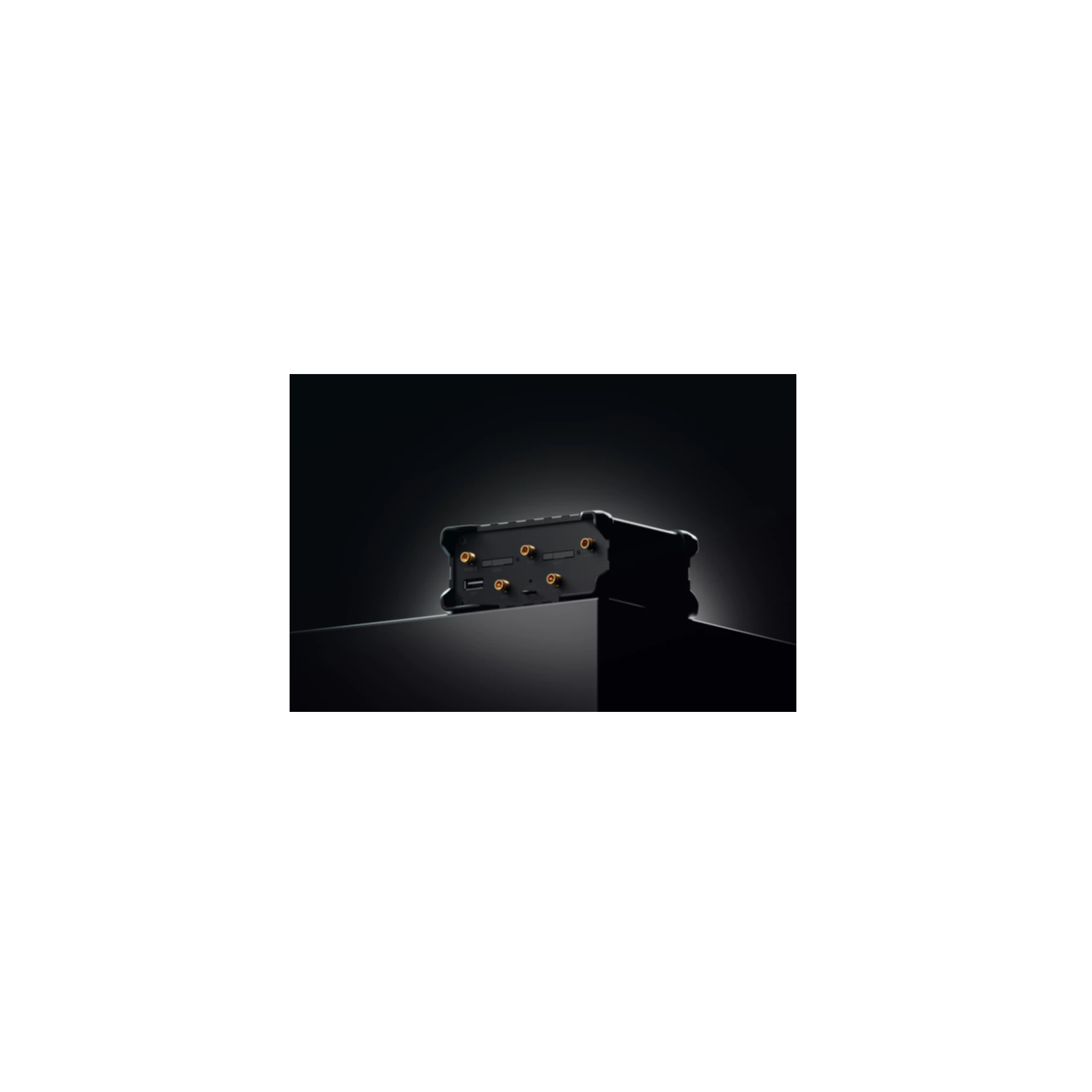A black electronic device with multiple ports and slots. It sits on a dark surface with a black background.