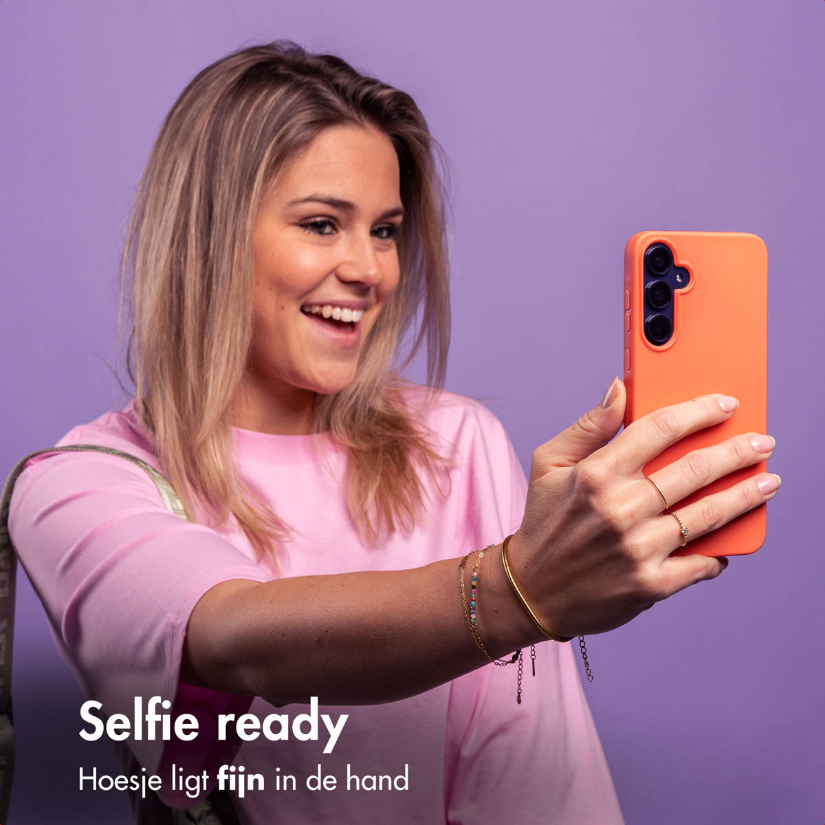 Eine Frau macht ein Selfie mit orangefarbener Handyhülle, lächelnd, auf lila Hintergrund.