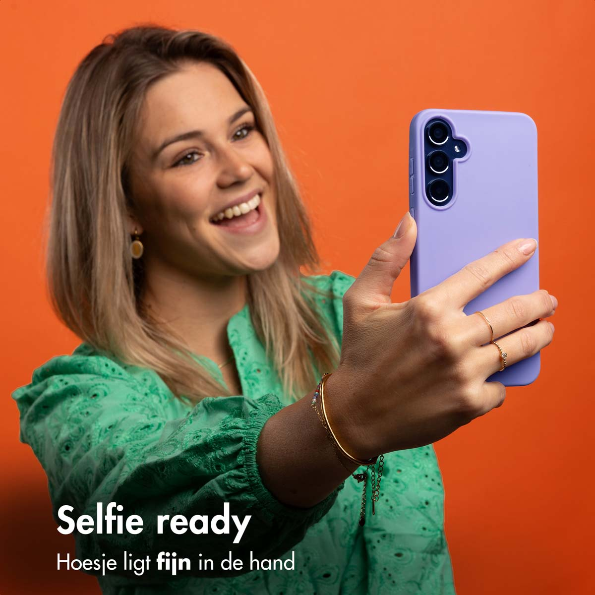 Eine Frau macht ein Selfie mit lila Handyhülle, lächelnd, auf orangefarbenem Hintergrund.