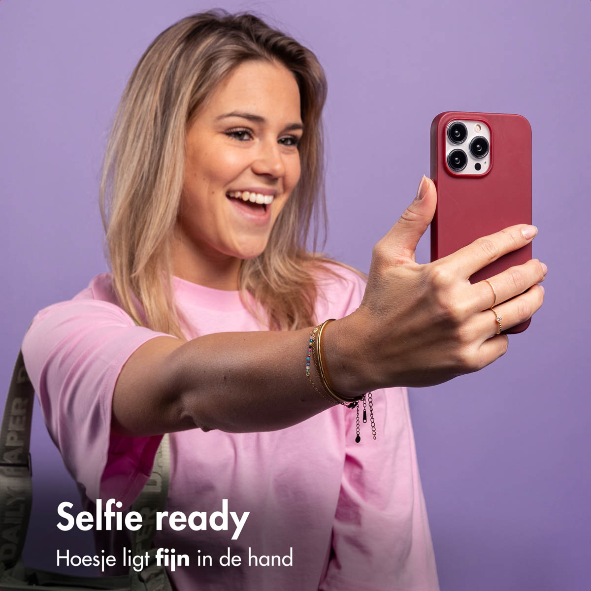 Frau macht ein Selfie mit einer weinroten Handyhülle. Sie lächelt. Der Hintergrund ist lila.