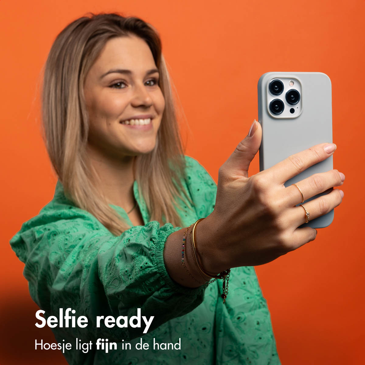 Frau macht Selfie mit grauer Handyhülle. Oranger Hintergrund.