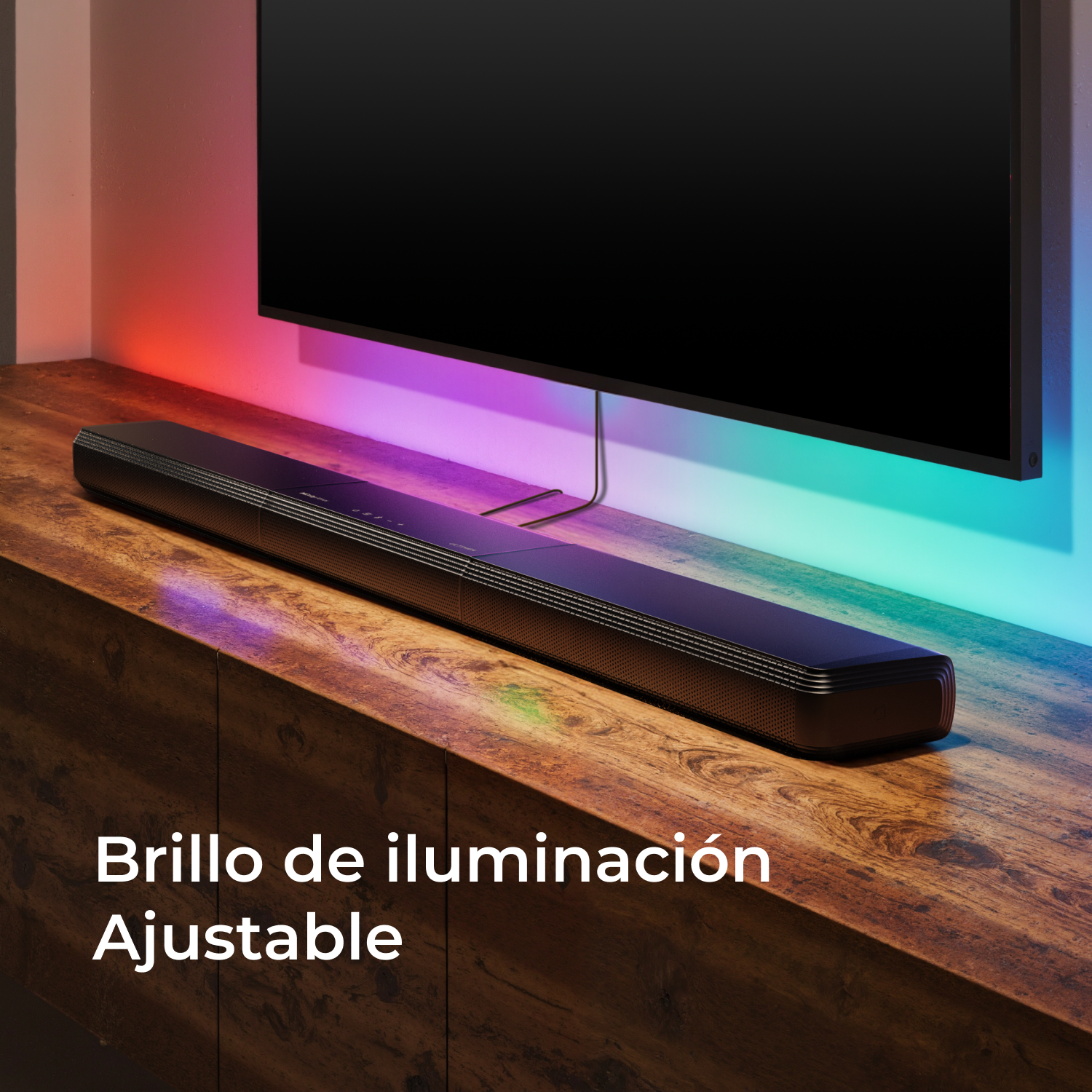 Una barra de sonido negra sobre un mueble de madera. Un televisor encima. El fondo está iluminado con colores.