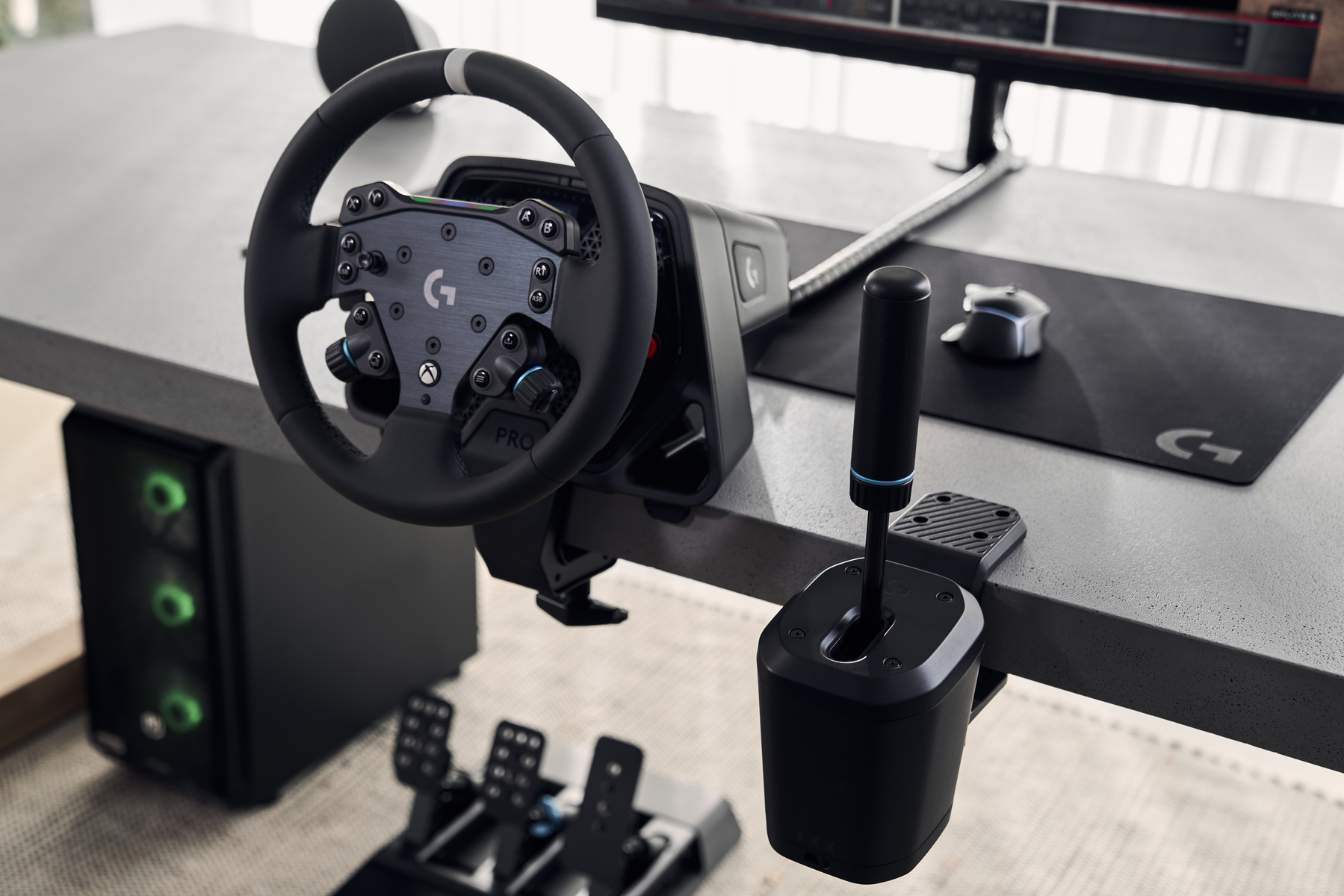 Un volante di gioco con cambio, pedali e monitor su una scrivania. Un case per computer a sinistra.