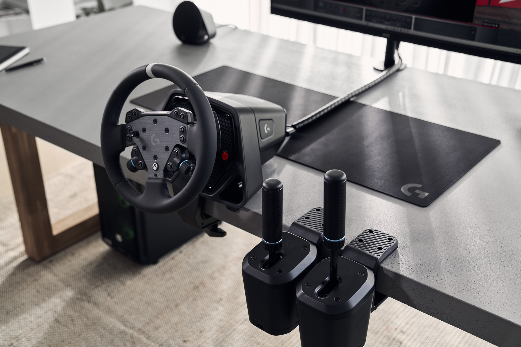 Un volante da corsa e un cambio sono su una scrivania. Un monitor di computer e un tappetino per il mouse nero sono visibili.