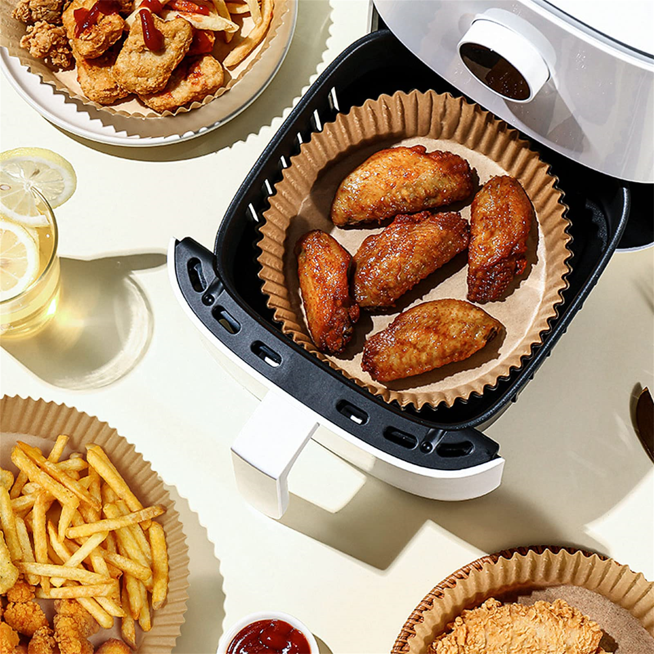 Heißluftfritteuse mit Hähnchenflügeln und Pommes, andere Lebensmittel sichtbar.