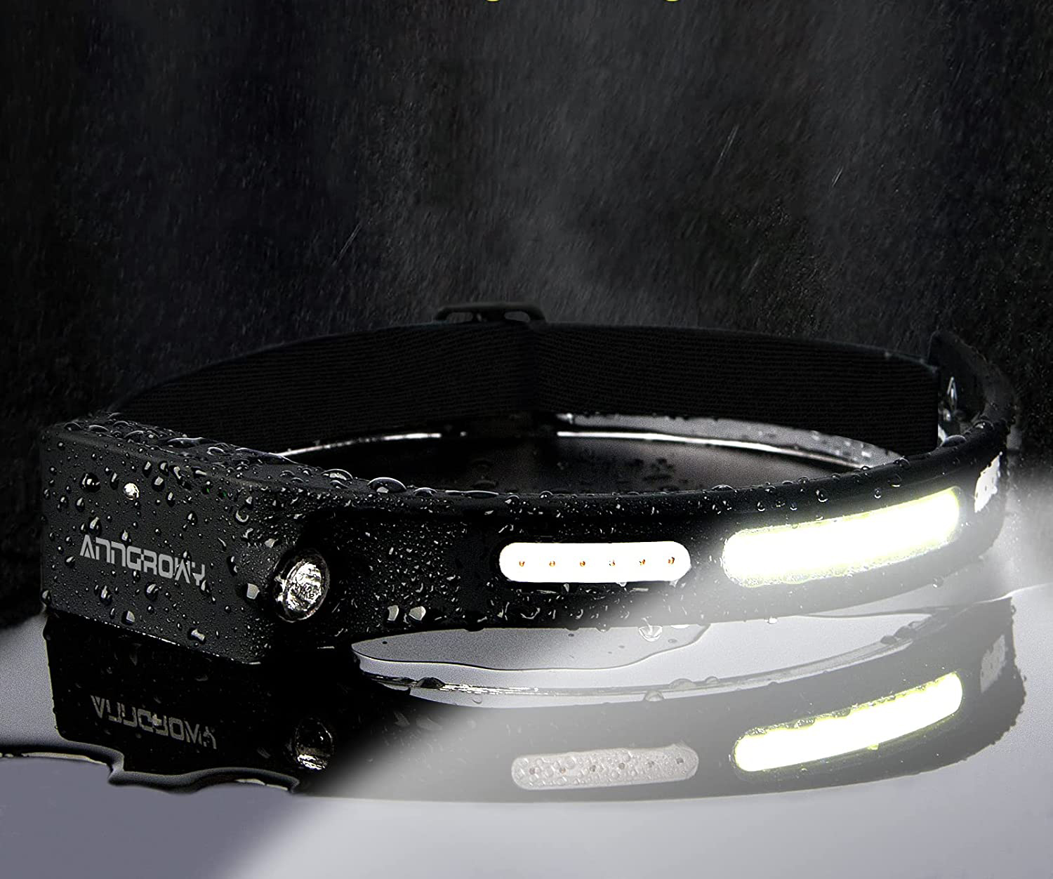 Eine schwarze Stirnlampe leuchtet und spiegelt sich auf einer nassen Oberfläche. Die Stirnlampe hat weiße Lichter und das Wort ANTIGROMY.