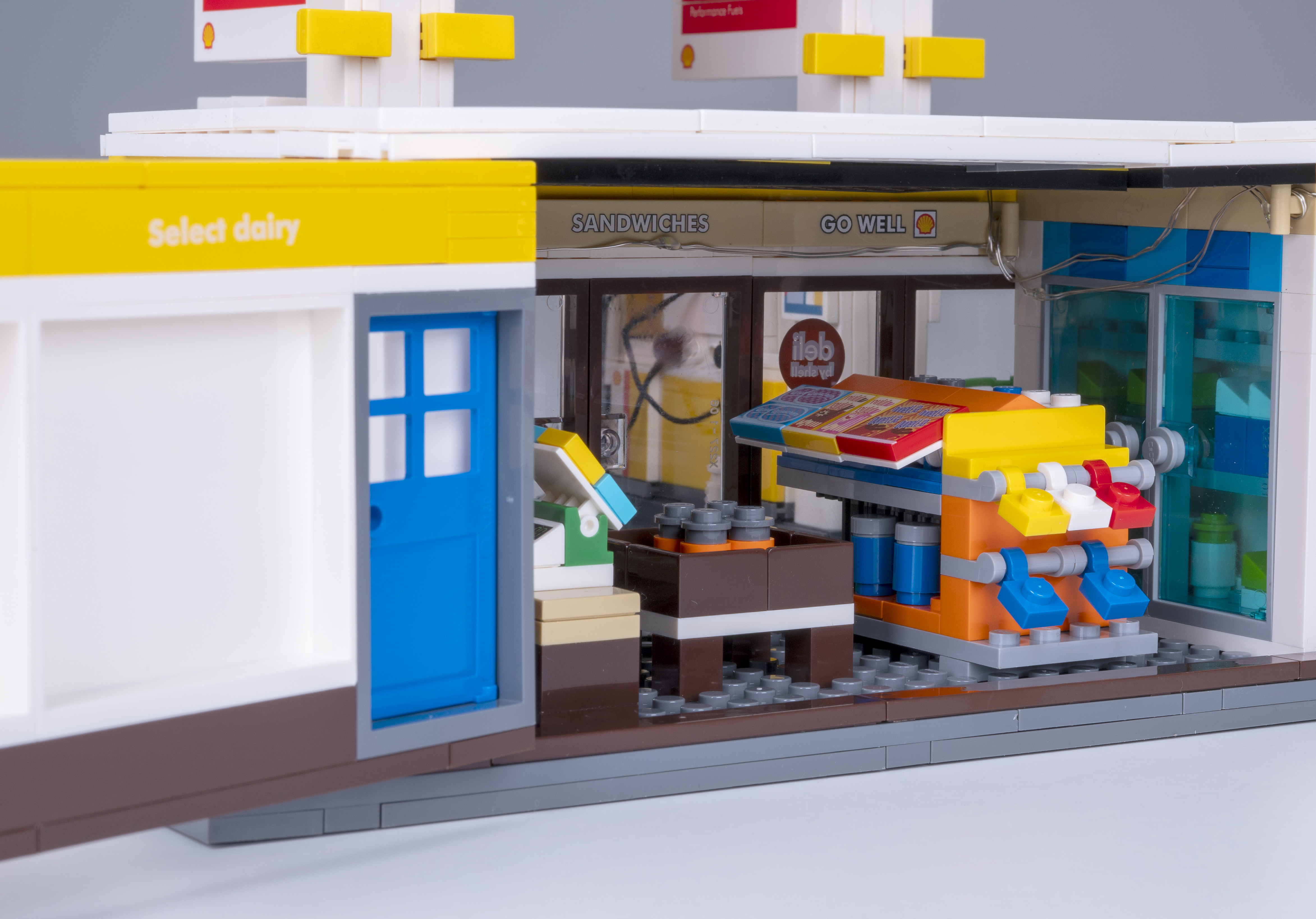 Ein Lego-Tankstelleninnenraum mit einer blauen Tür, einer Ausstellung von Sandwiches und Getränken und einem Schild mit 'Go Well'.