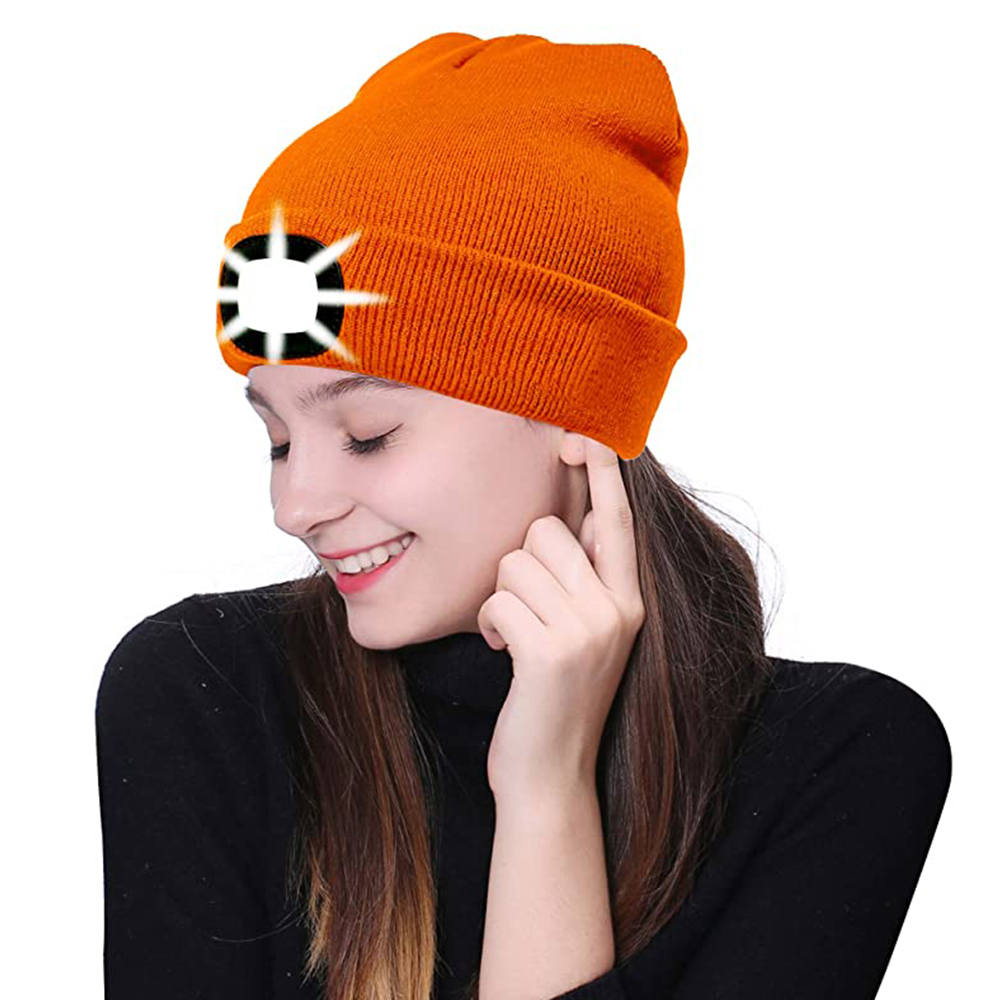 Eine Frau mit einer orangefarbenen Beanie-Mütze mit weißem Licht, lächelnd und zeigt auf das Ohr.