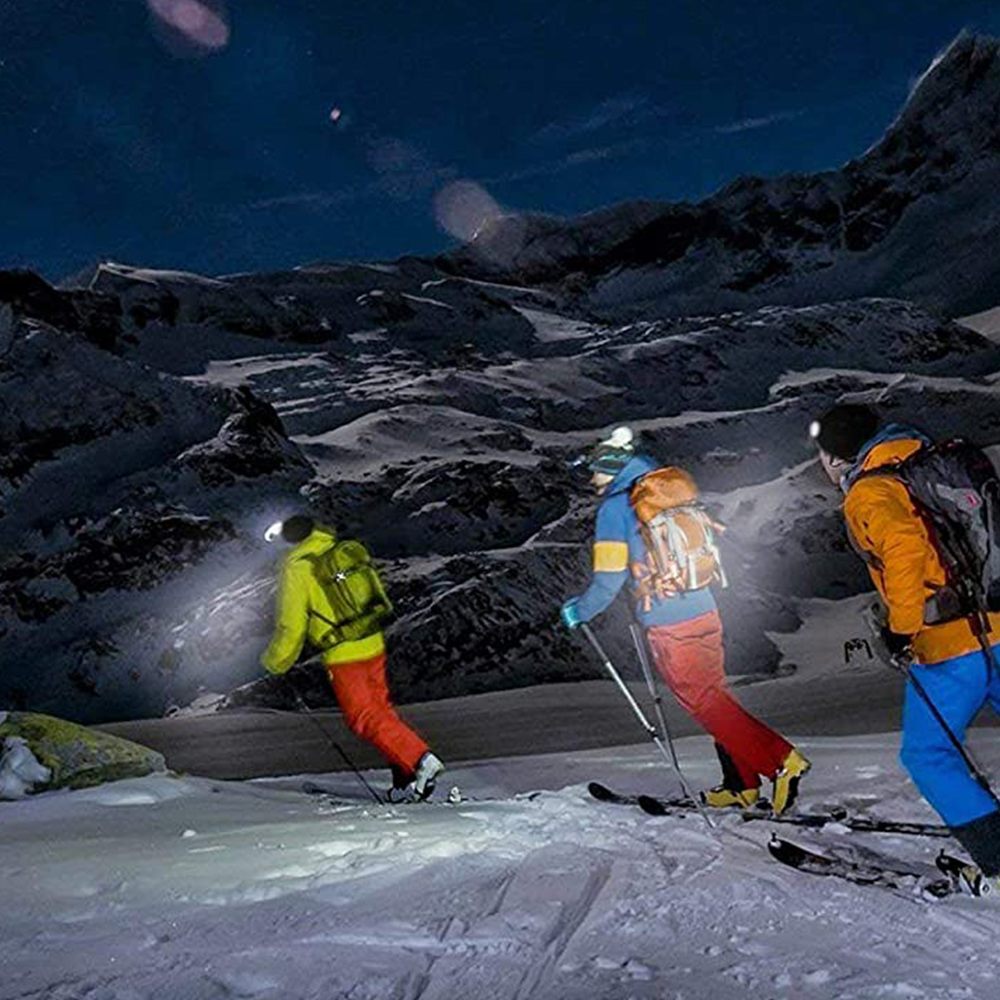 Skifahrer mit Stirnlampen auf einem schneebedeckten Berg unter einem Nachthimmel.