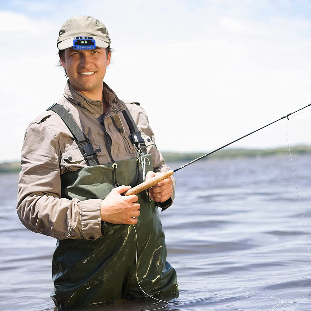 Ein Mann fischt und trägt eine Kappenleuchte. Er steht im Wasser, hält eine Angelrute und lächelt.