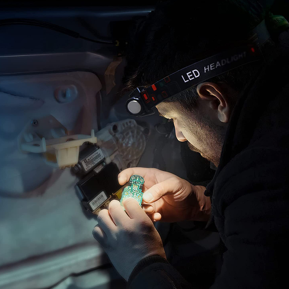 Eine Person arbeitet an einer Leiterplatte und trägt eine Stirnlampe, die die Elektronik beleuchtet.