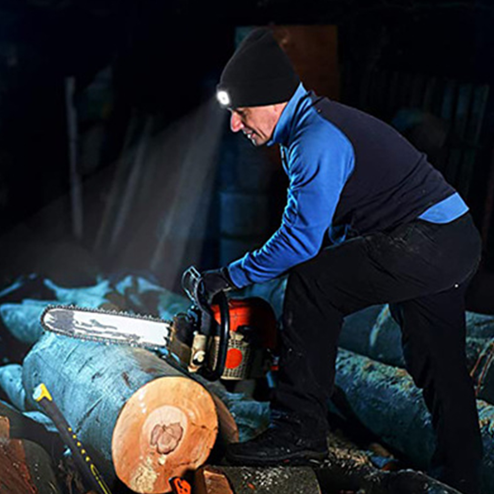 Ein Mann mit einer schwarzen Mütze mit Licht, der mit einer Kettensäge Holz schneidet. Dunkler Hintergrund.