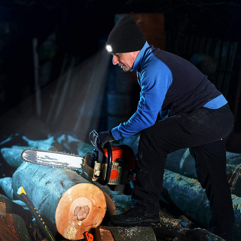 Mann mit schwarzer Mütze und hellem Licht schneidet Holz mit einer Kettensäge.
