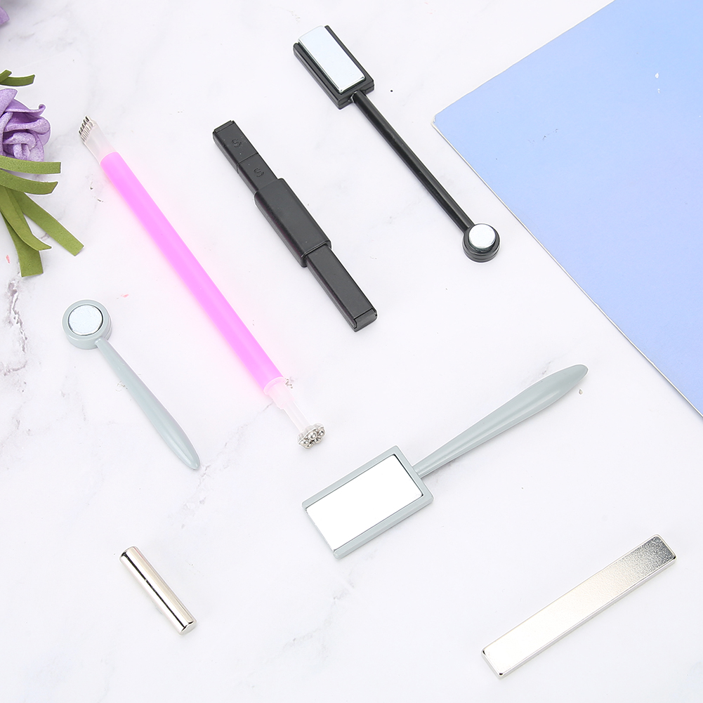 Verschiedene Nagelkunstwerkzeuge, darunter Magnetstäbe und ein rosa Werkzeug, sind auf einer weißen Oberfläche angeordnet.
