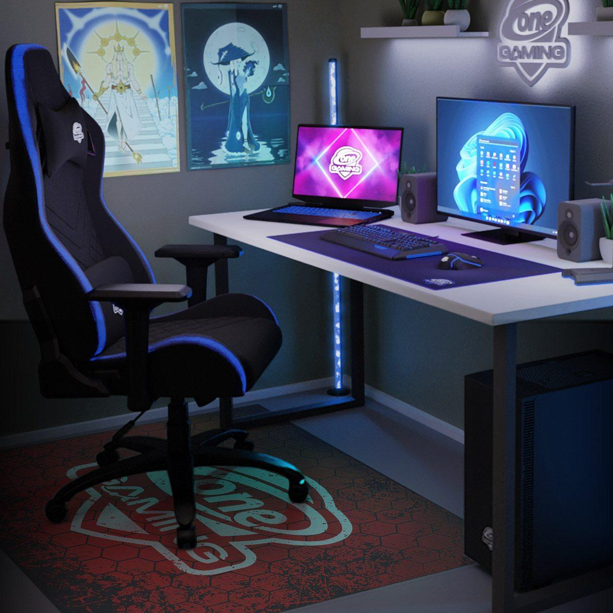 Gaming-Setup: schwarz-blauer Stuhl, Schreibtisch mit Monitor, Laptop, Tastatur, Mauspad und Lautsprecher, Poster an der Wand.