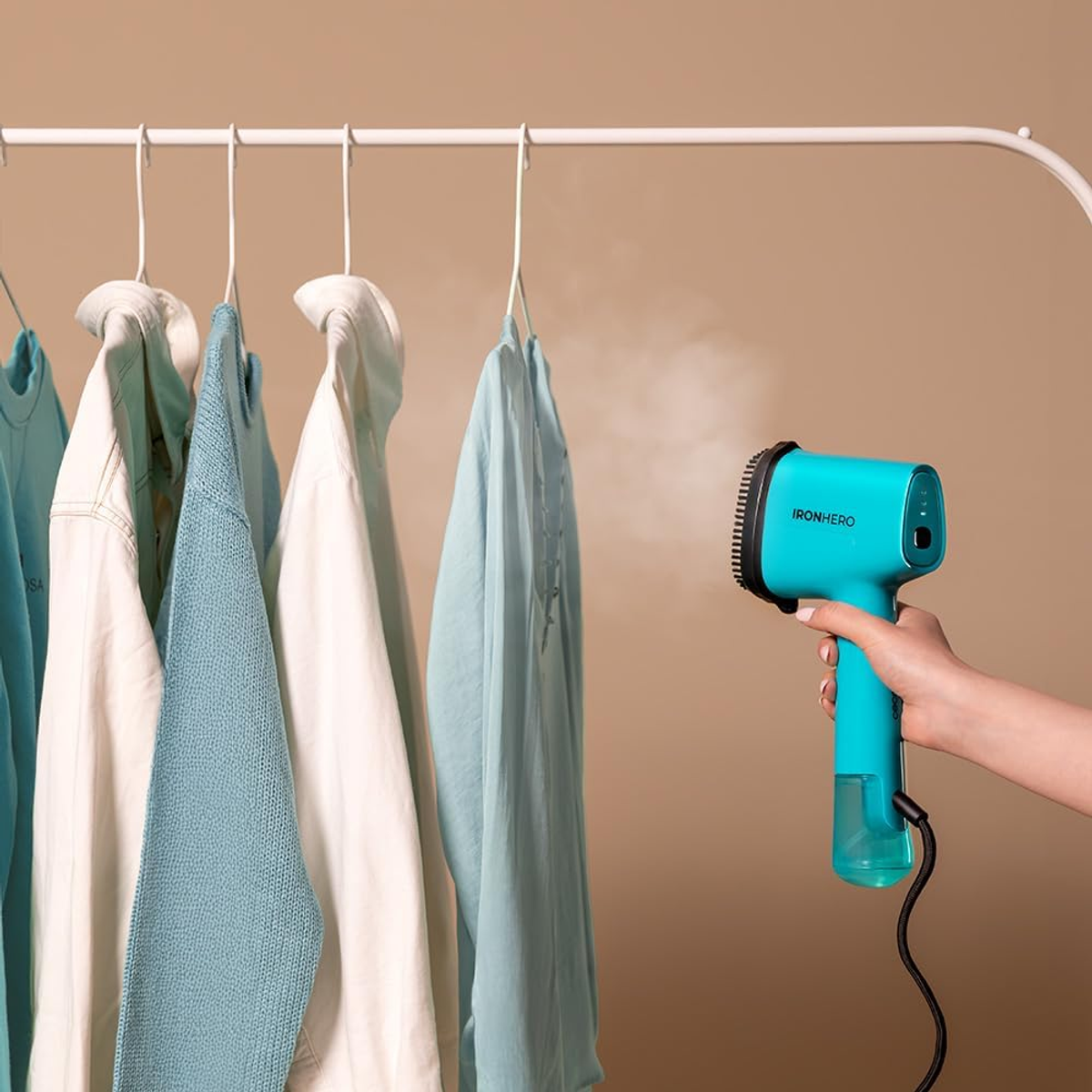 Una persona usa un vaporizzatore a mano blu per stirare i vestiti appesi a un attaccapanni.