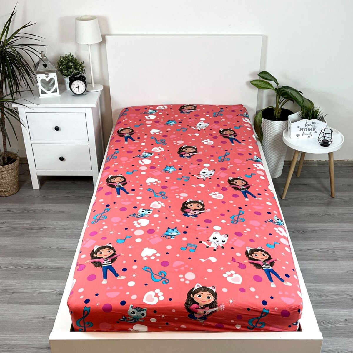 Ein rosa Bettlaken mit Zeichentrickfiguren, Noten und Katzenköpfen. Es liegt auf einem weißen Bettrahmen.
