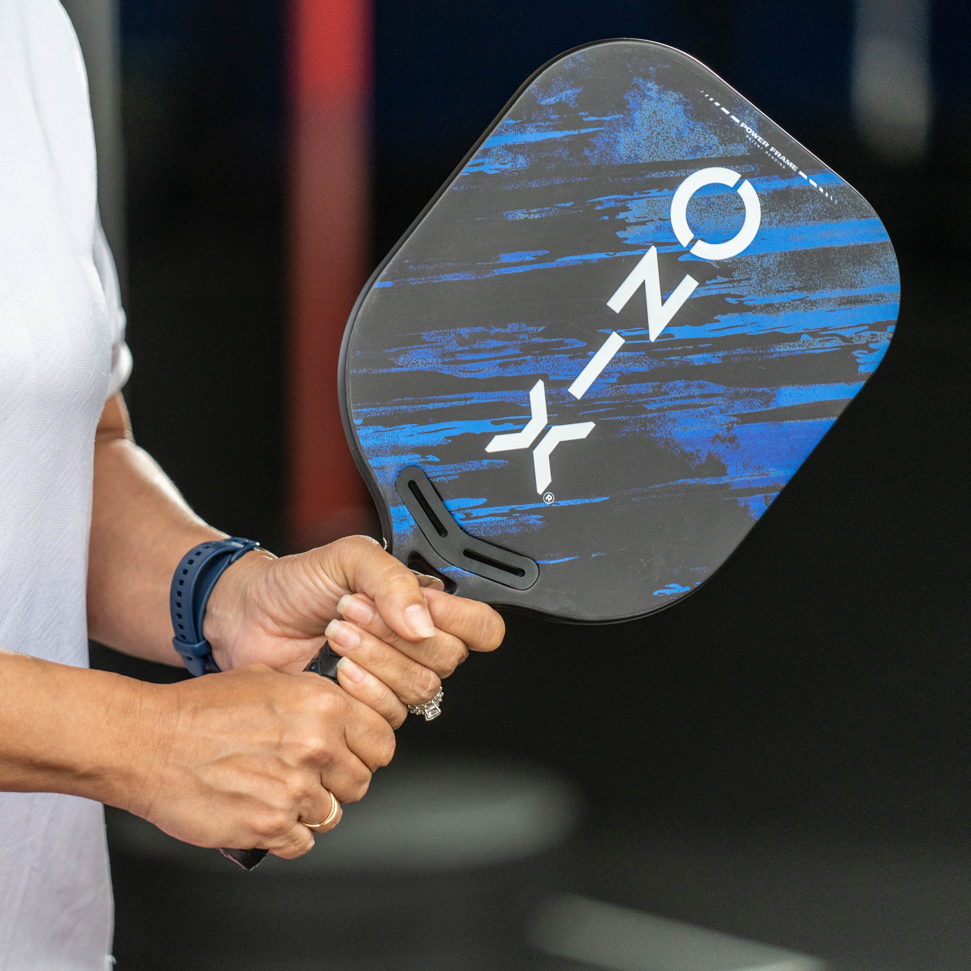 Eine Frau hält einen schwarz-blauen ONIX Pickleball-Schläger. Ihre blaue Uhr und ihr Ring sind sichtbar.