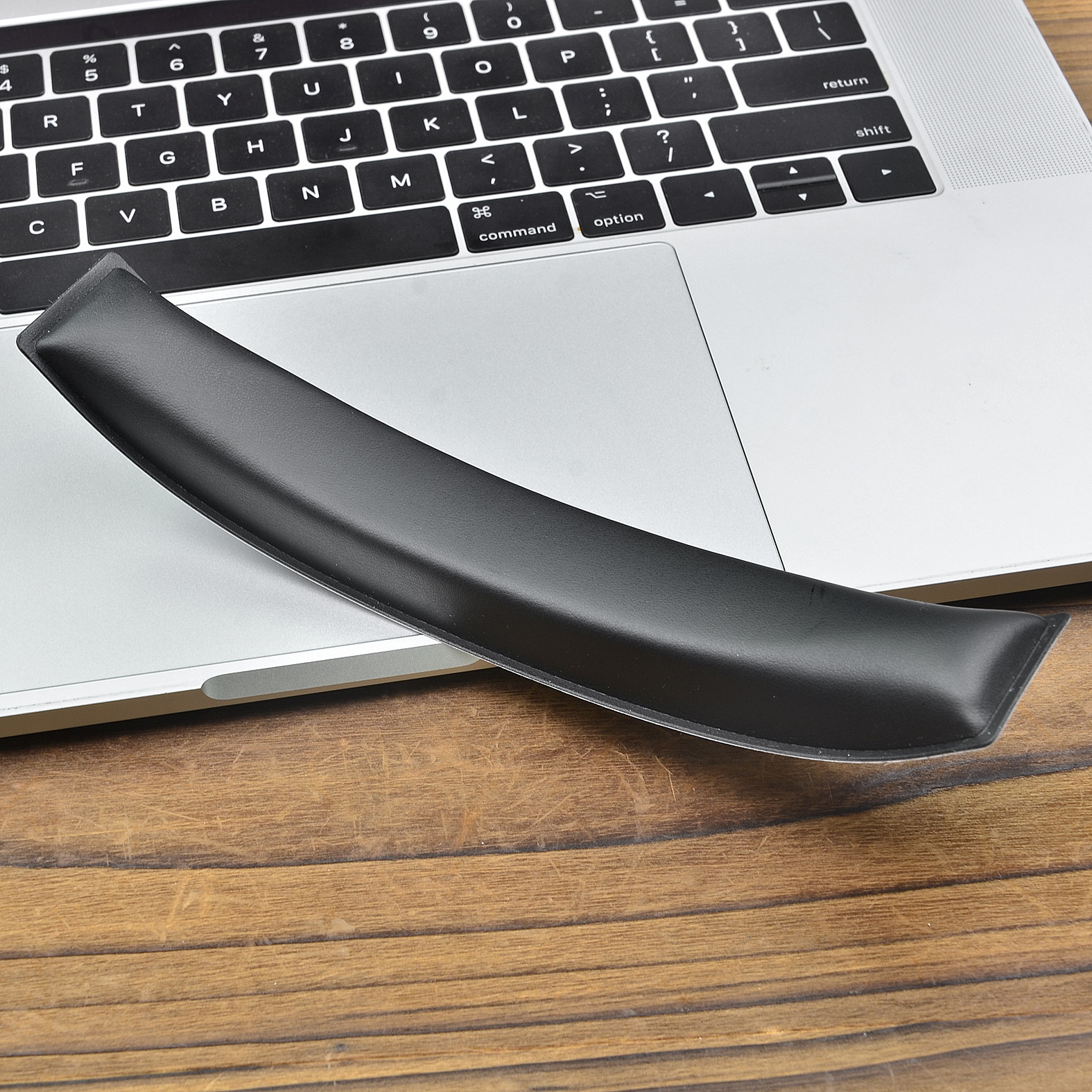 Poggiapolsi nero e curvo su un laptop argentato appoggiato su un tavolo di legno. Il laptop è aperto.