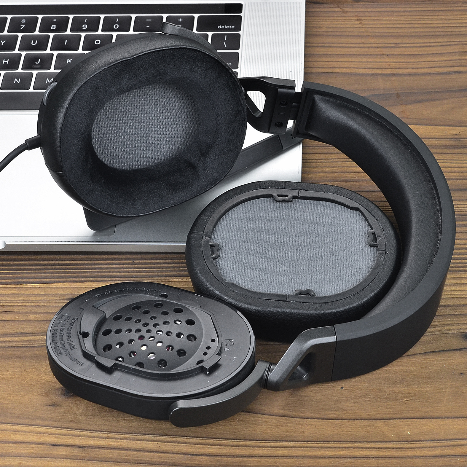 Cuffie smontate. Padiglioni auricolari staccati dalla fascia, componenti interni visibili. Posizionate su una superficie in legno.
