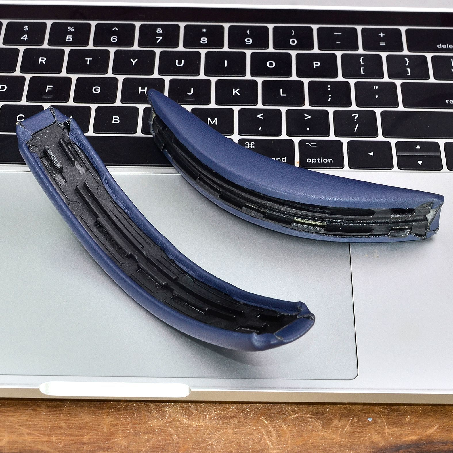 Zwei blaue Kopfhörer-Ohrmuscheln liegen auf einer silbernen Laptop-Tastatur.