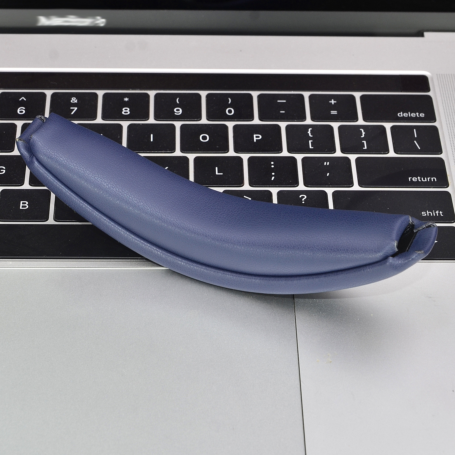 Eine blaue Kopfhörer-Ohrmuschel liegt auf einer silbernen Laptop-Tastatur.