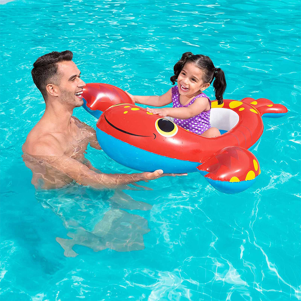 Ein Mann und ein Mädchen im Pool. Das Mädchen sitzt in einem krabbenförmigen Schwimmreifen und lächelt.