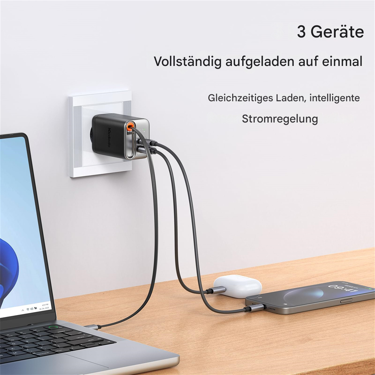 Ladegerät, das drei Geräte auflädt: Laptop, Telefon und Ohrhörer.