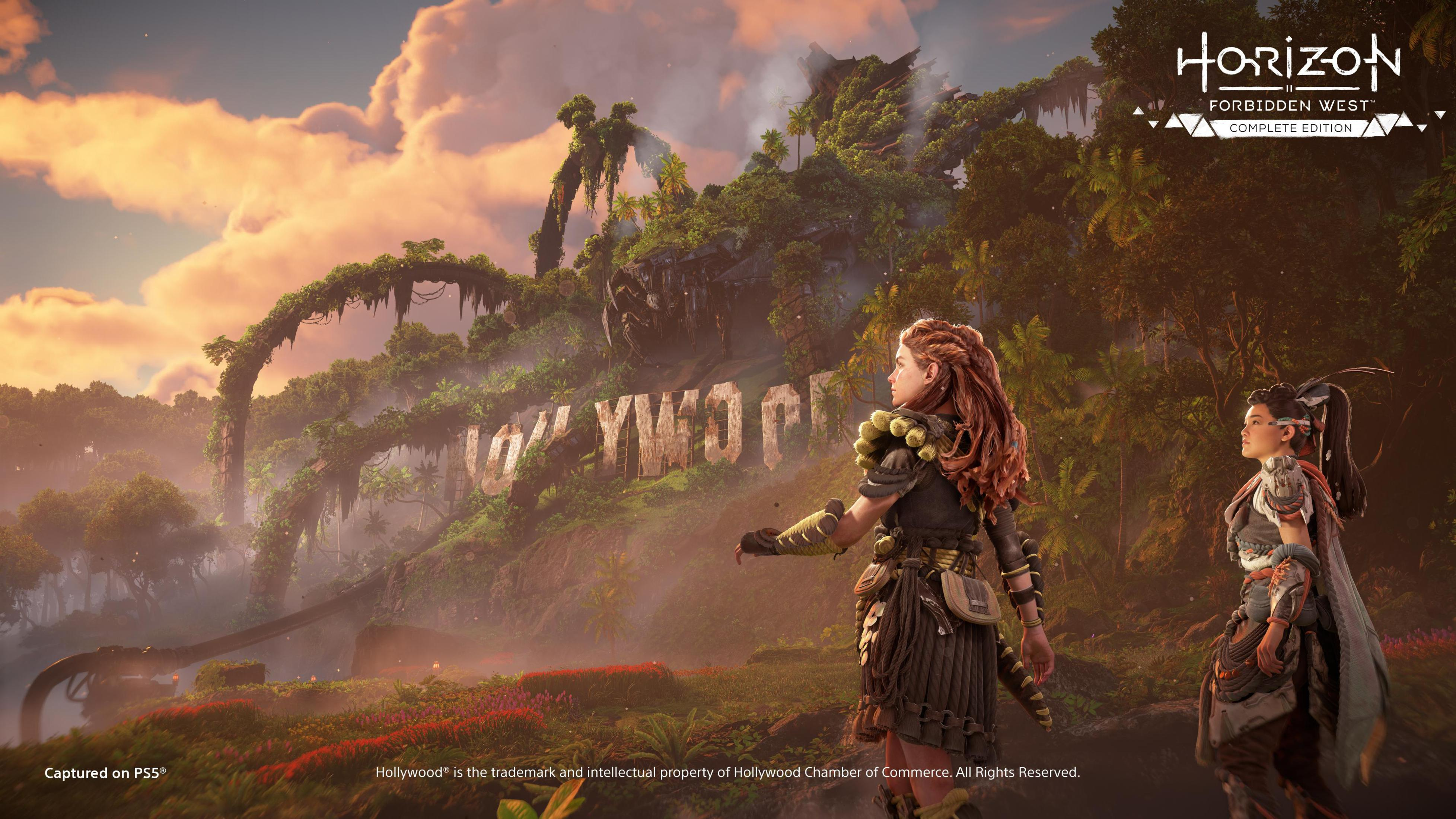 Zwei Frauen stehen in der Nähe des Hollywood-Schriftzugs. Der Himmel ist bewölkt. Bäume und Berge sind sichtbar.