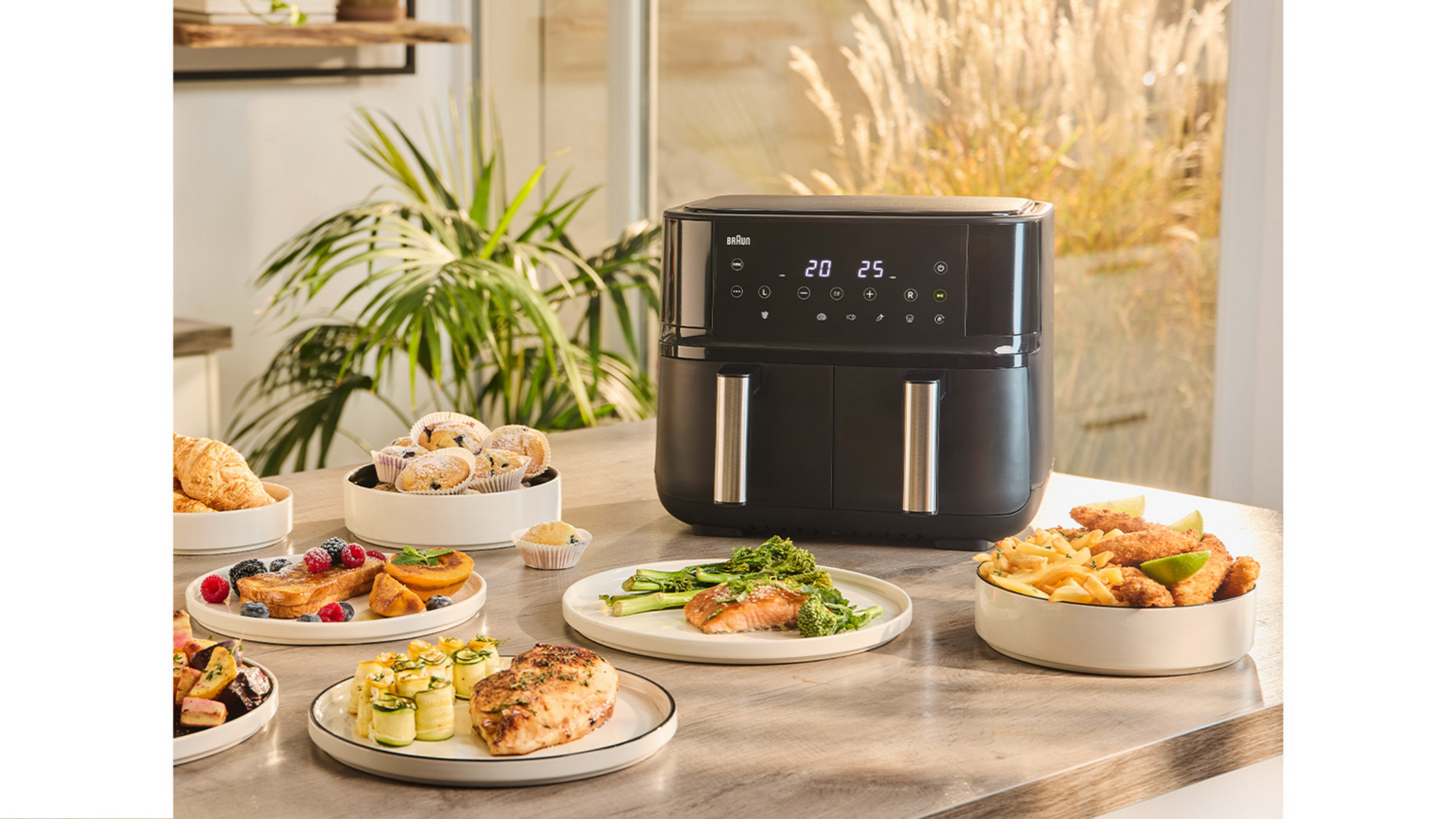 Zwarte airfryer met eten op een tafel. Gerechten zijn gebak, groenten en vlees.