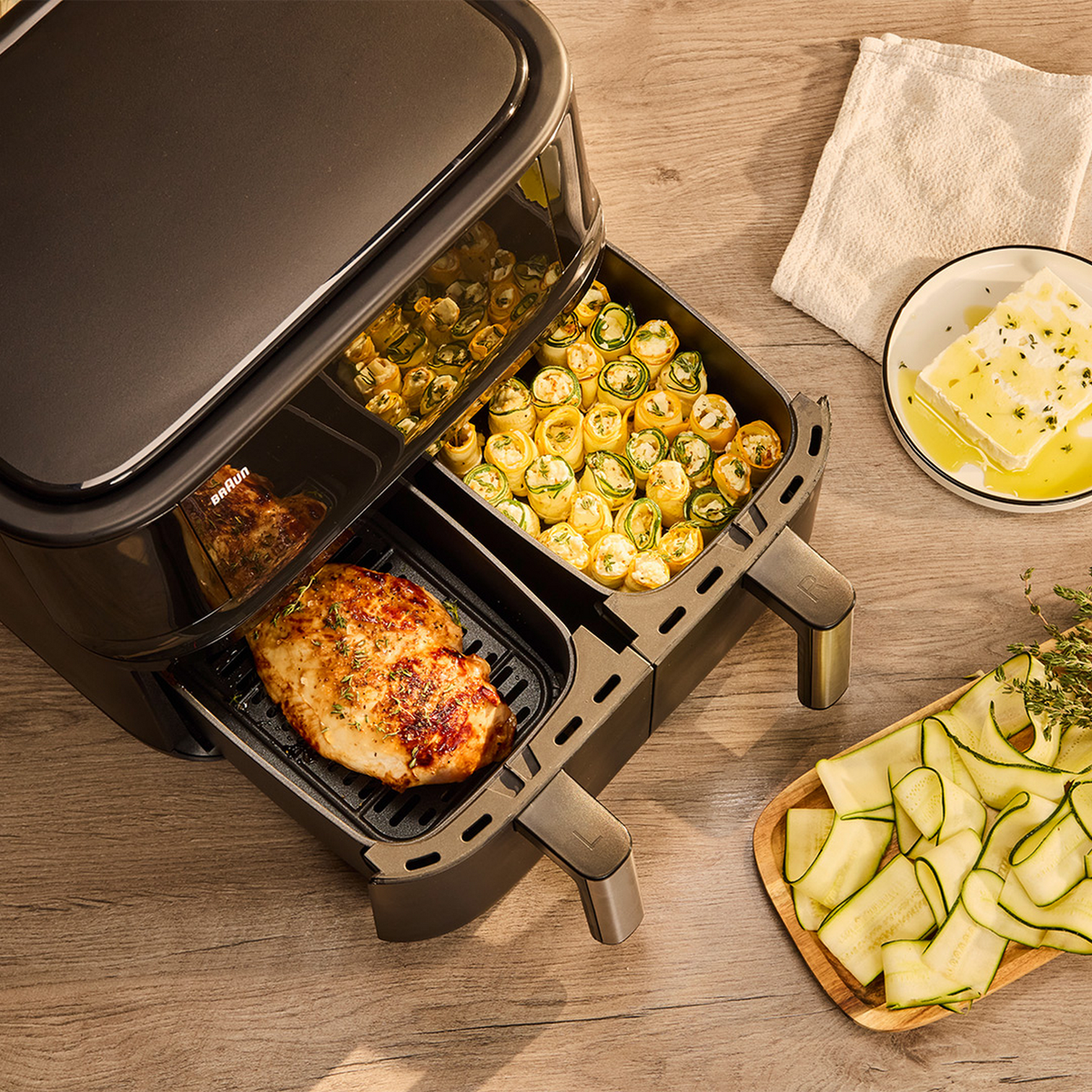 Airfryer met eten erin. Er zijn kipfilets, courgette en andere gekookte items.