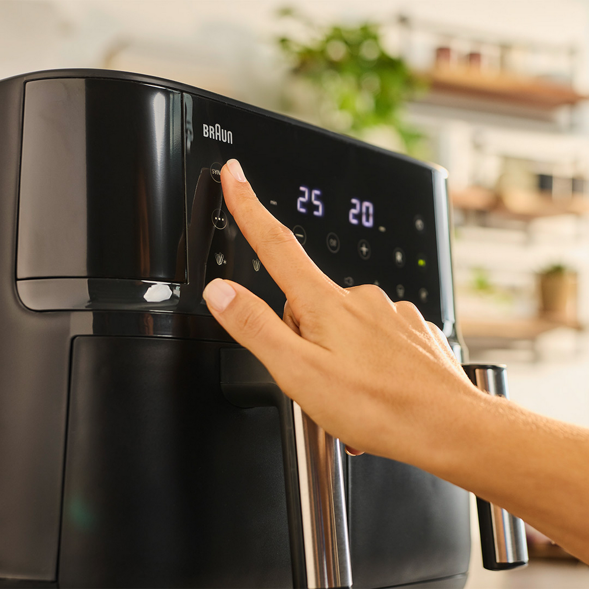 Een hand die op een knop van een zwarte airfryer drukt, met een digitaal display.
