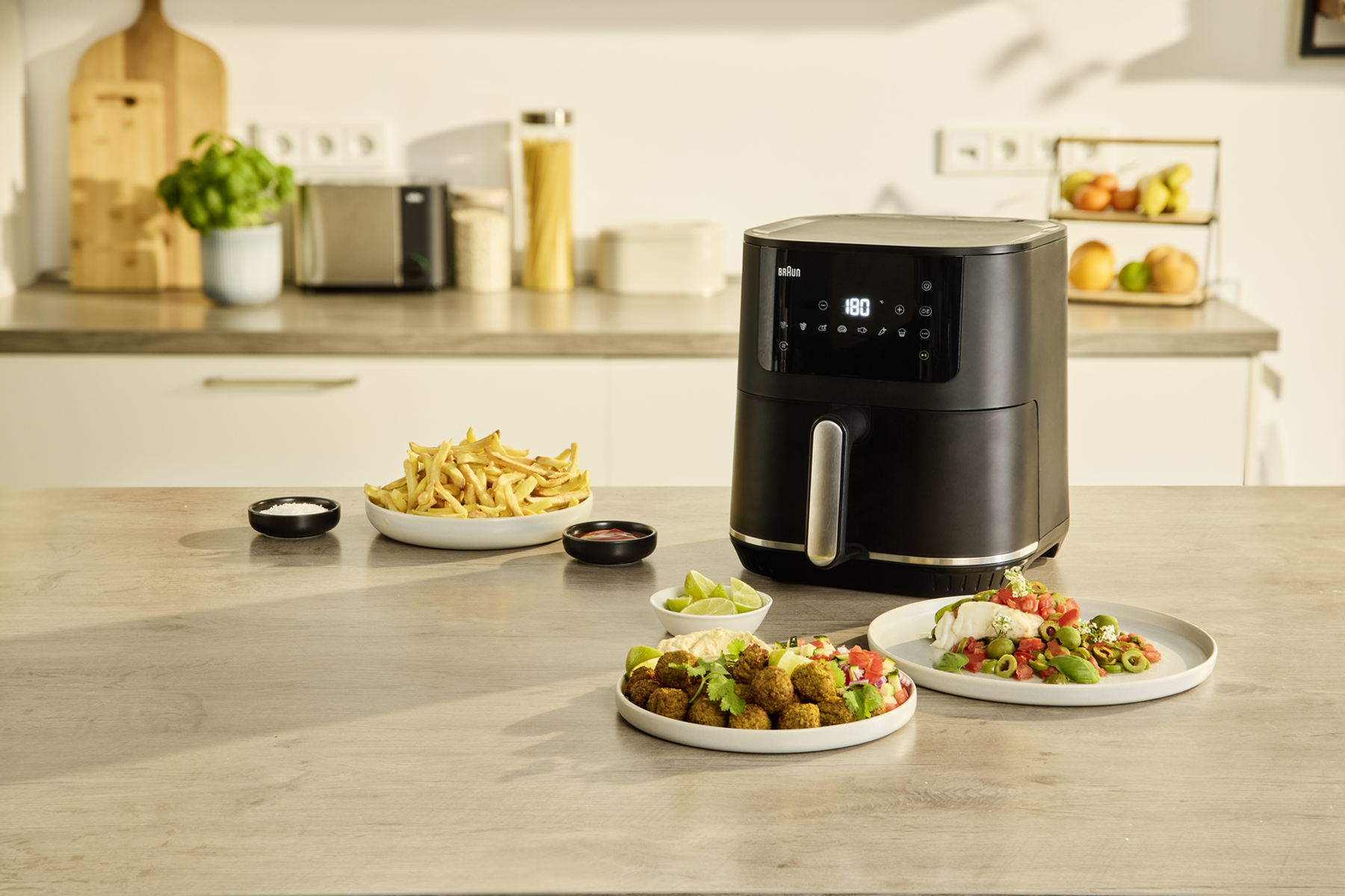 Czarna frytownica na blacie, z talerzami jedzenia. Frytki, falafel i sosy z przodu.