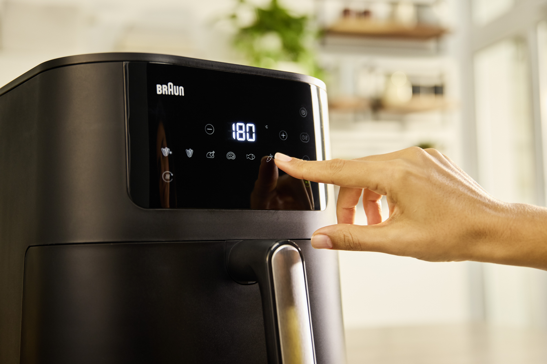 Ręka naciskająca przycisk na czarnej frytkownicy, pokazująca wyświetlacz temperatury.