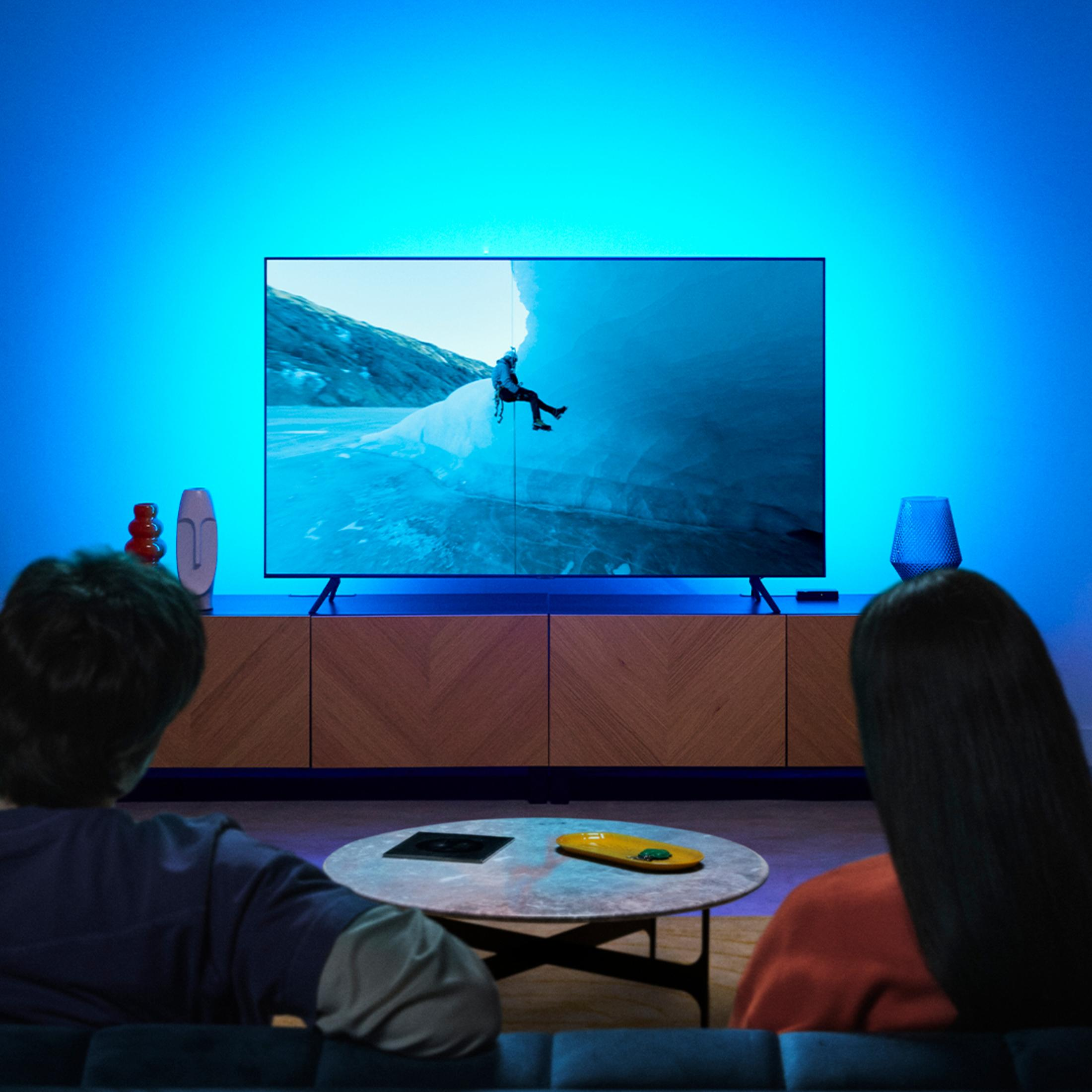 Bir çift, bir oturma odasında mavi ortam aydınlatması ile TV'de bir dağcıyı izliyor.