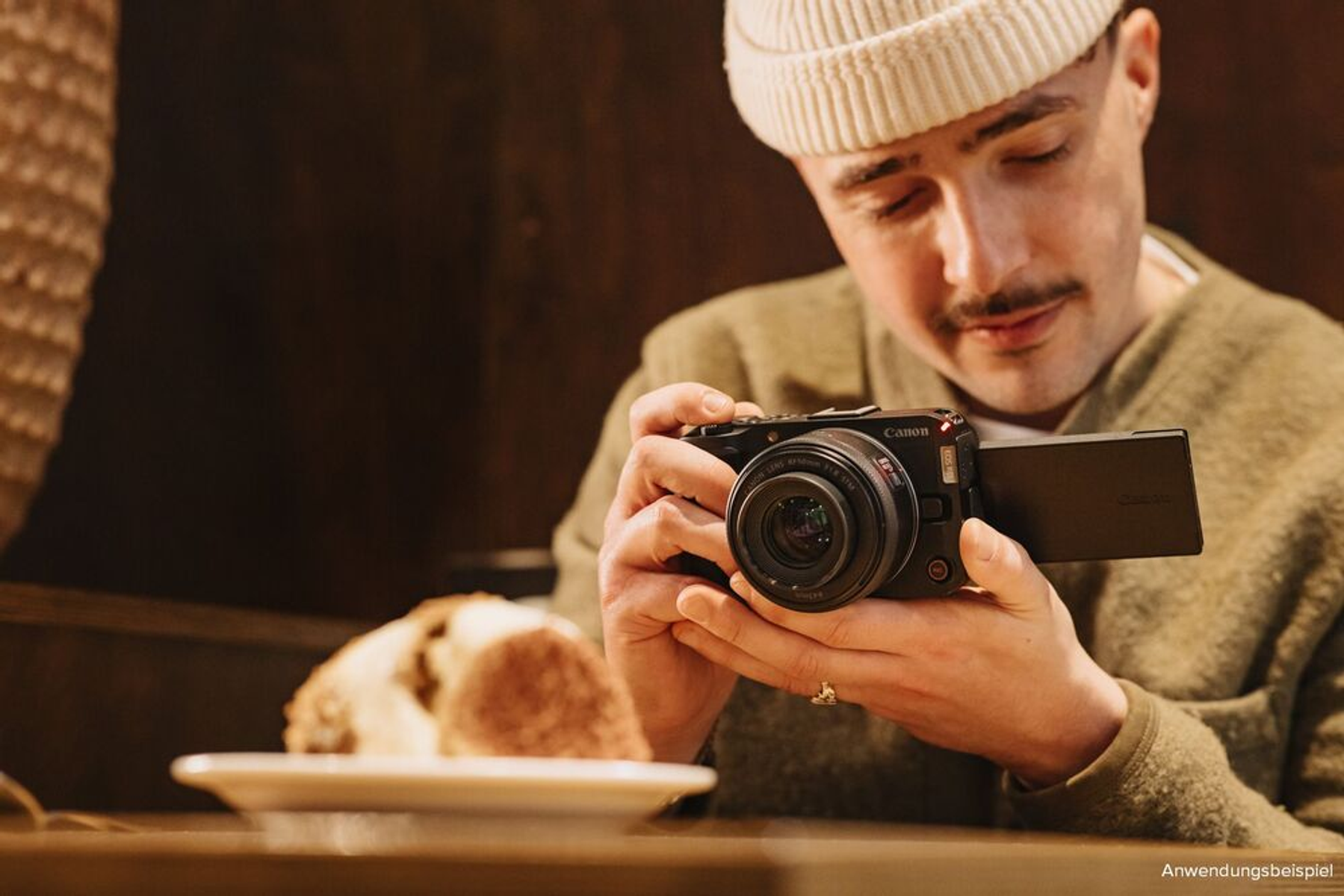 Mężczyzna trzyma czarny aparat, patrząc na ekran siedząc przy stole.