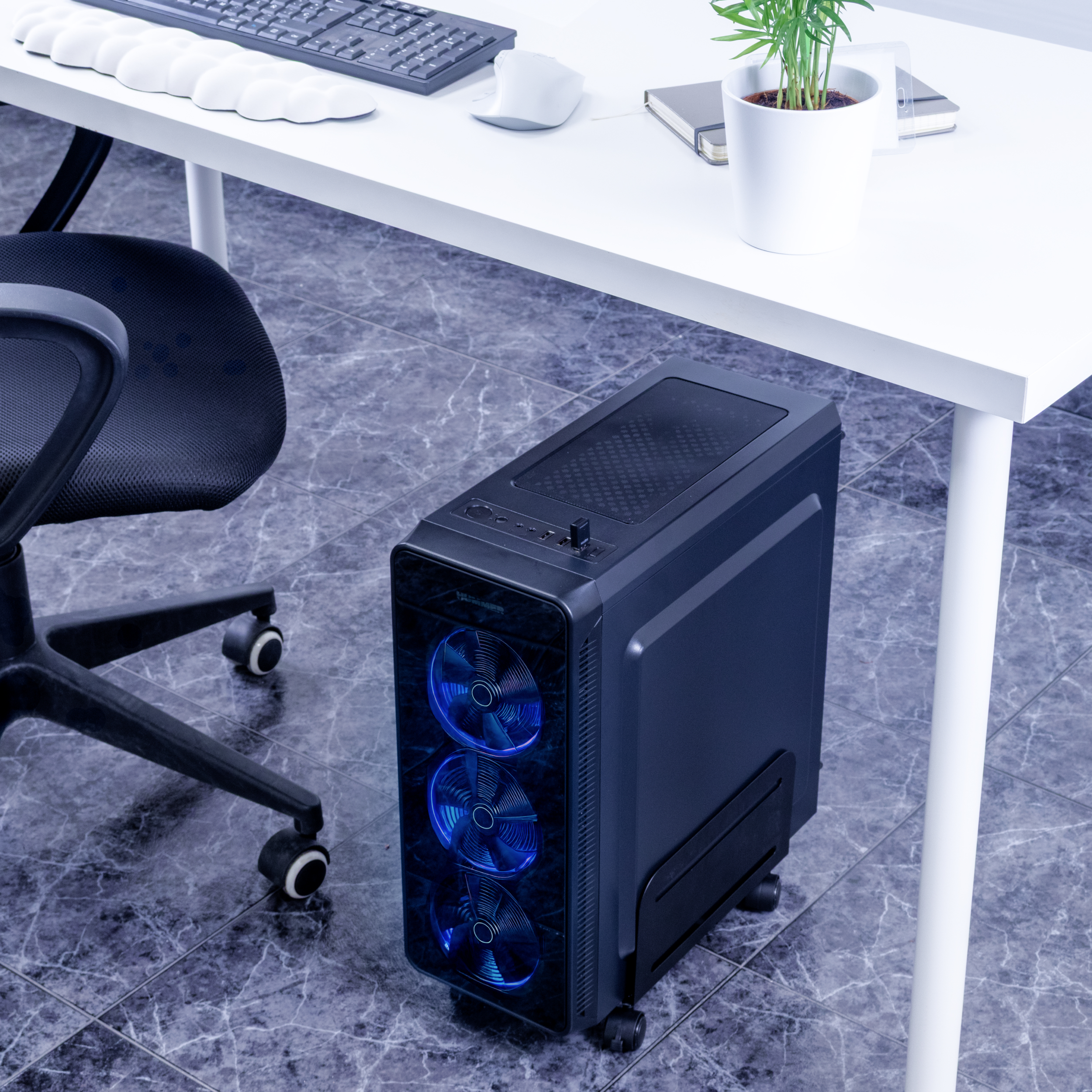 Una torre de computadora negra con luces azules. Escritorio con teclado y ratón y una silla negra.