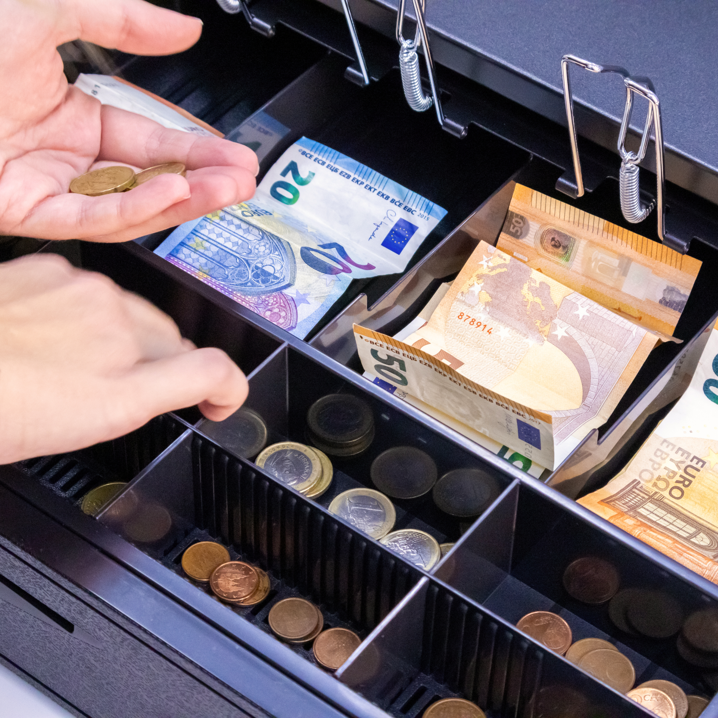 Cajón registrador abierto, con efectivo y monedas. Manos organizando el dinero.