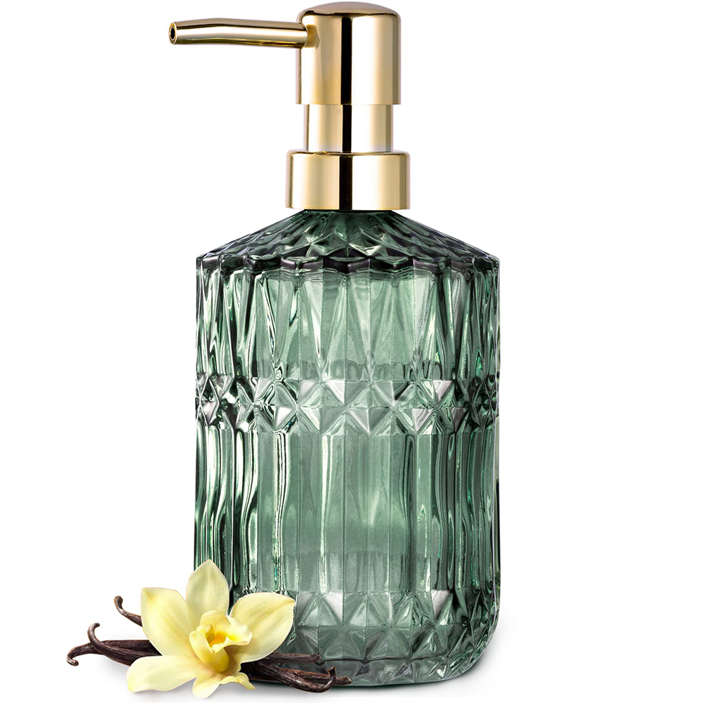 Ein grüner Glas-Seifenspender mit goldener Pumpe. Eine gelbe Blume und Vanilleschoten liegen am Boden.