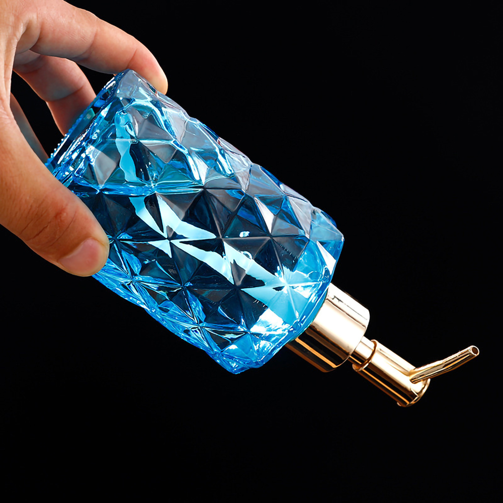 Eine Hand hält einen blauen, rautenförmigen Seifenspender vor schwarzem Hintergrund. Goldene Pumpe.