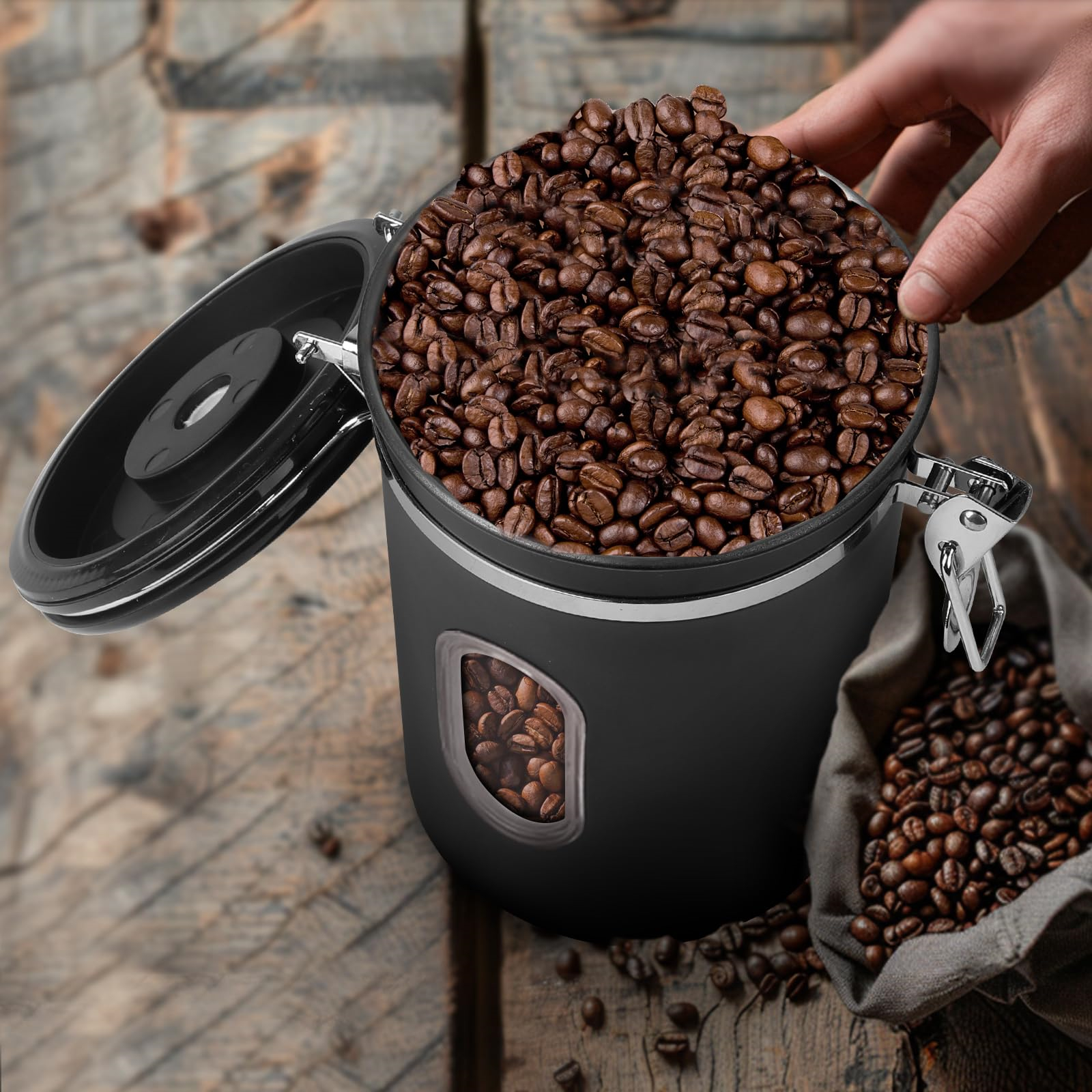 Ein schwarzer Kaffeebehälter ist geöffnet und mit Kaffeebohnen gefüllt. Eine Tüte und einige Bohnen sind ebenfalls vorhanden.