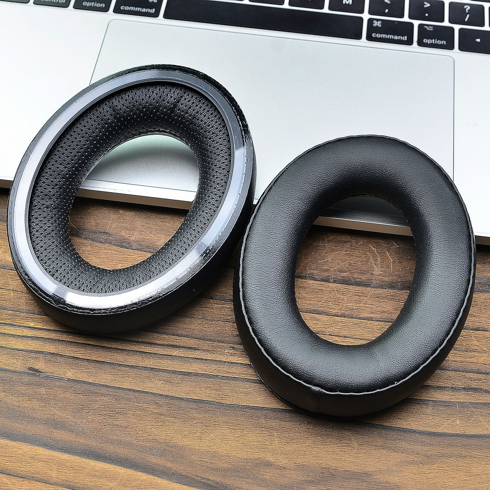 Due cuscinetti auricolari neri e rotondi per cuffie si trovano su una superficie di legno accanto a un laptop, uno con rete interna visibile.