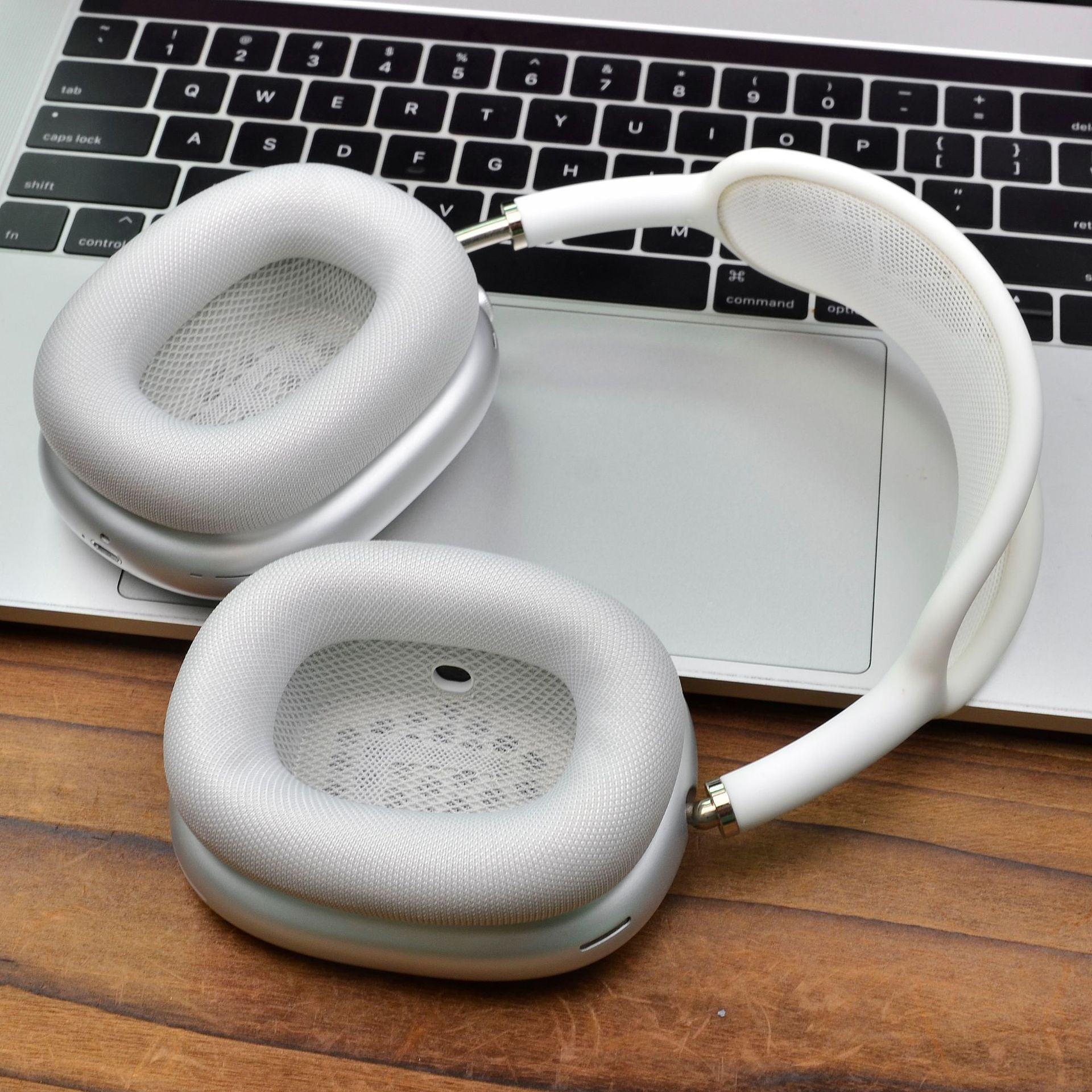 Due cuffie grigie su un laptop. Le cuffie sono aperte e il tavolo di legno è visibile.