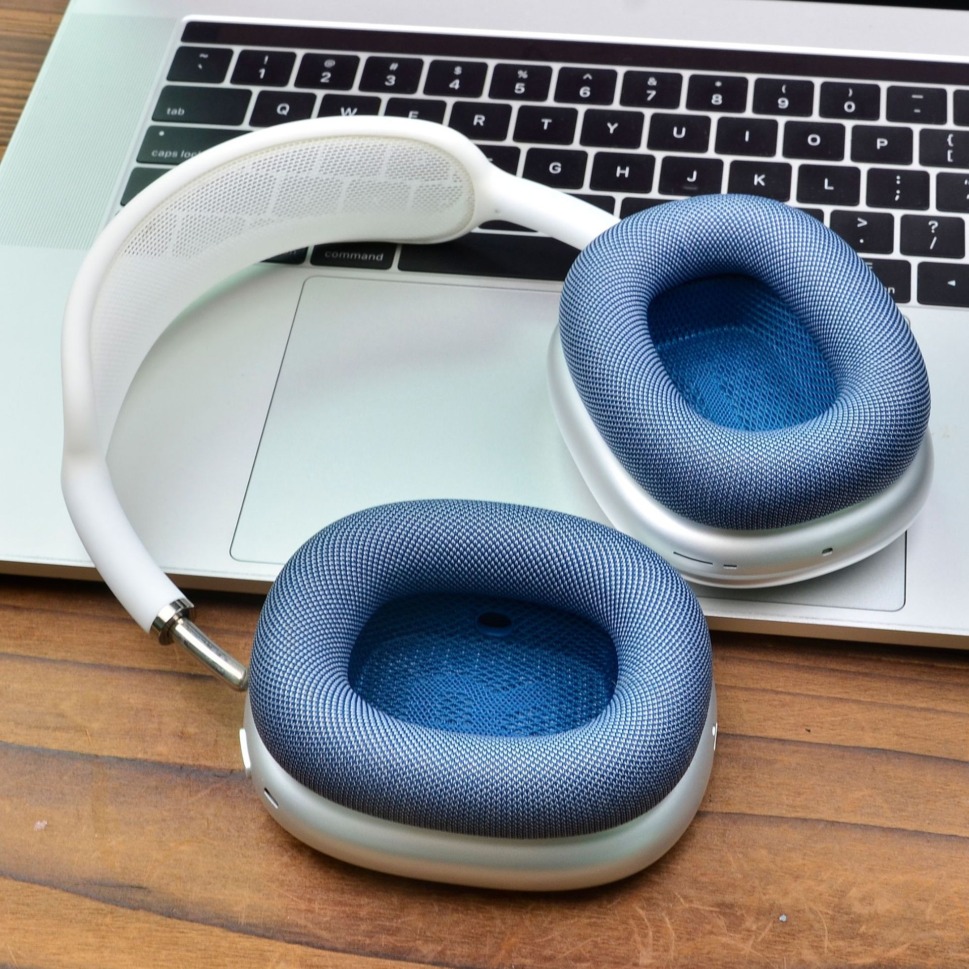 Cuffie bianche con padiglioni blu su una tastiera di un laptop e superficie in legno. Le cuffie sono aperte.