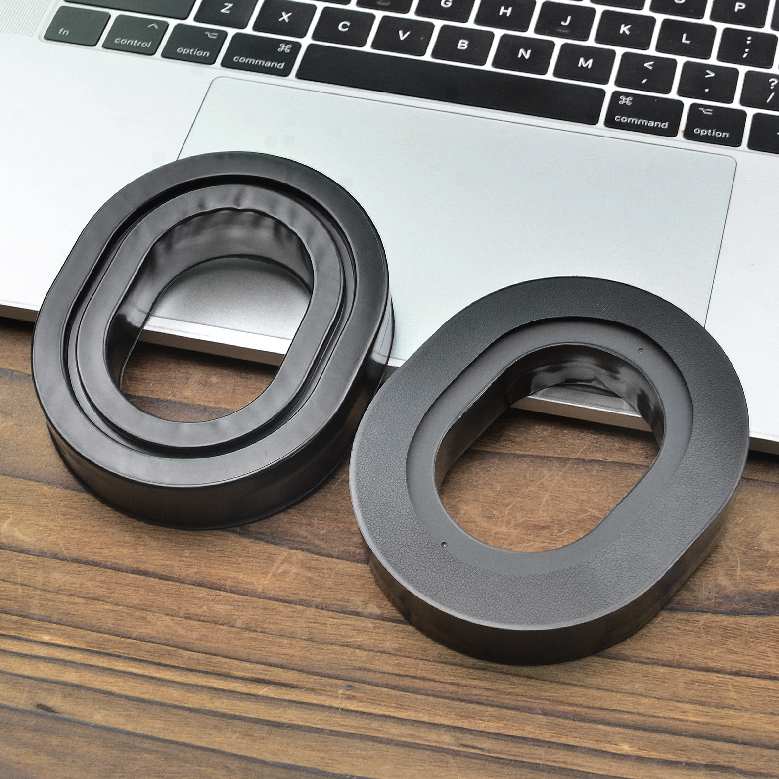 Due inserti in schiuma neri a forma ovale su una superficie in legno, vicino a una tastiera di un laptop.