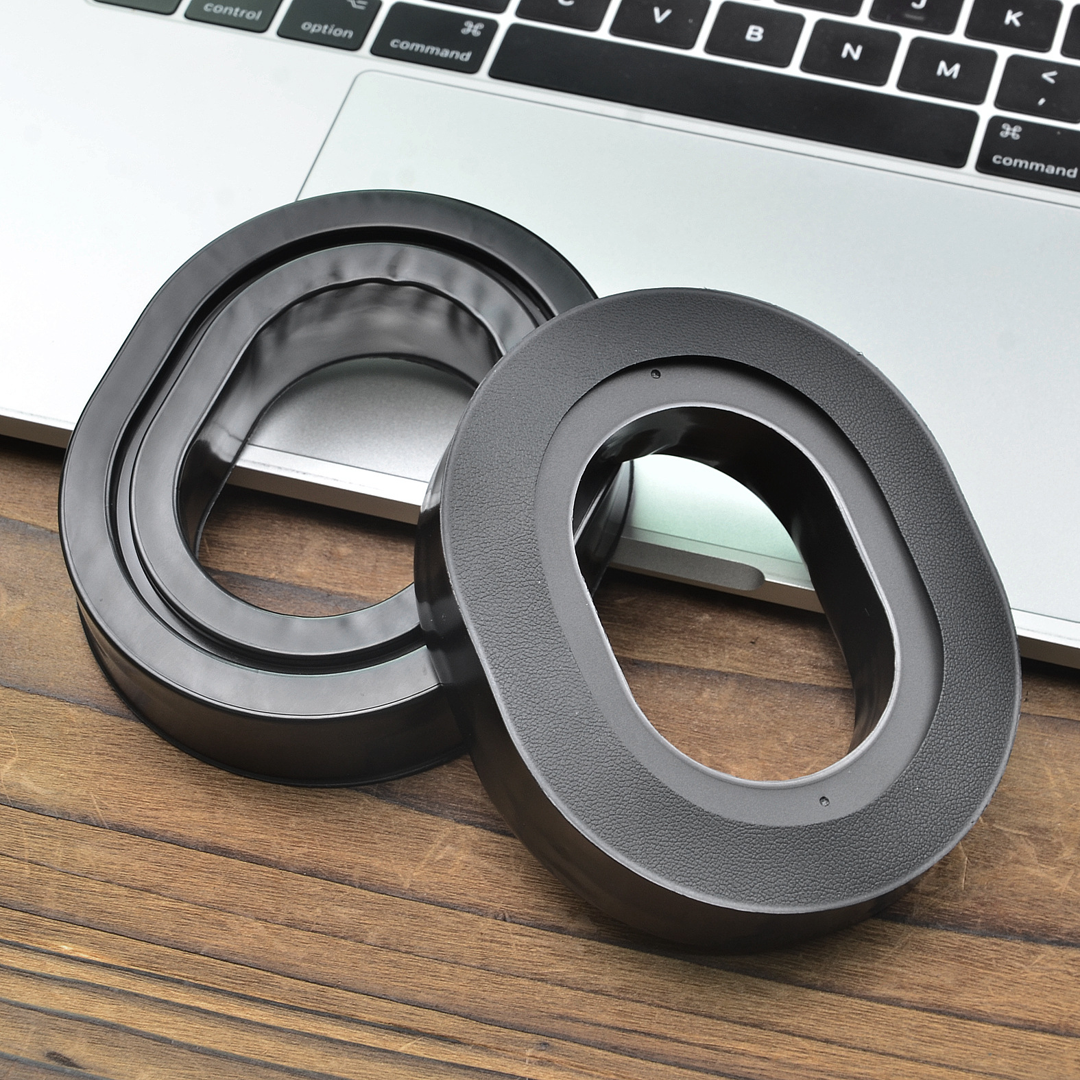 Due inserti in schiuma neri ovali su legno, accanto a un laptop, uno dentro l'altro.