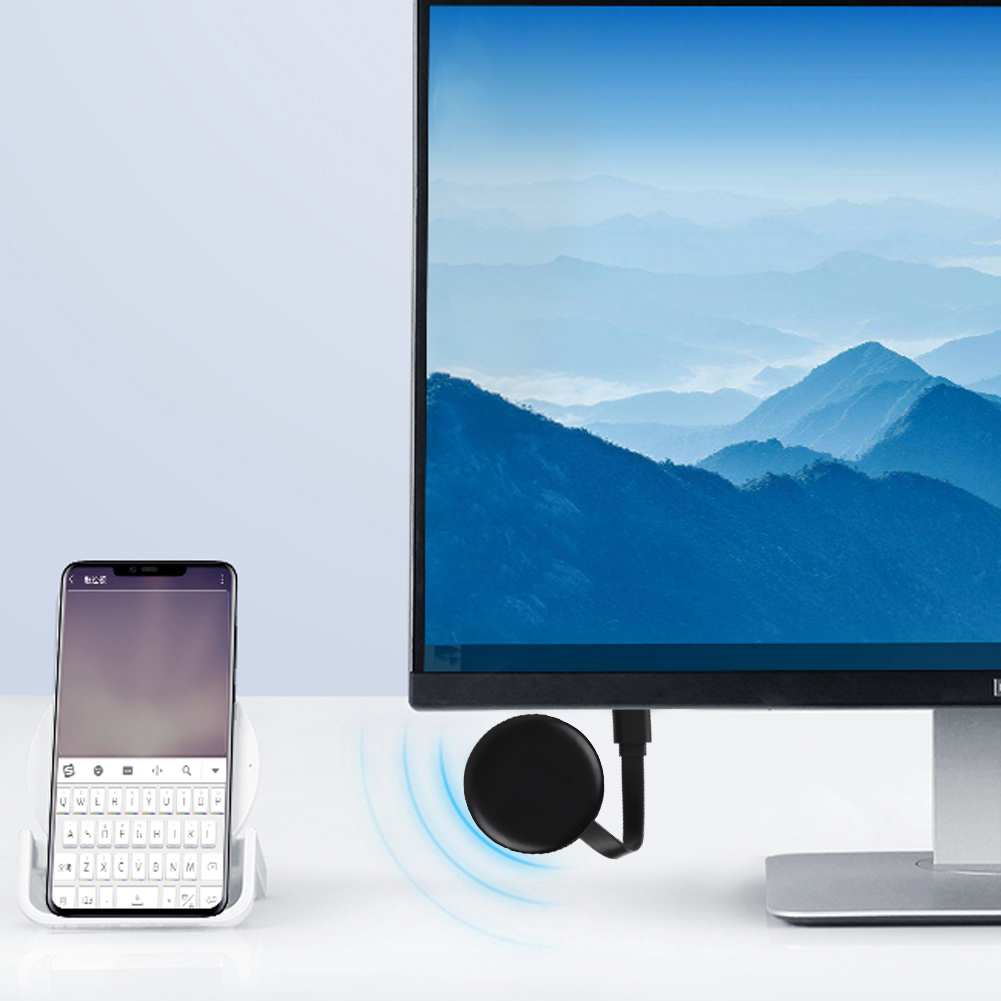Ein Smartphone liegt auf einem kabellosen Ladegerät neben einem Monitor. Ein schwarzes Gerät ist mit dem Monitor verbunden.