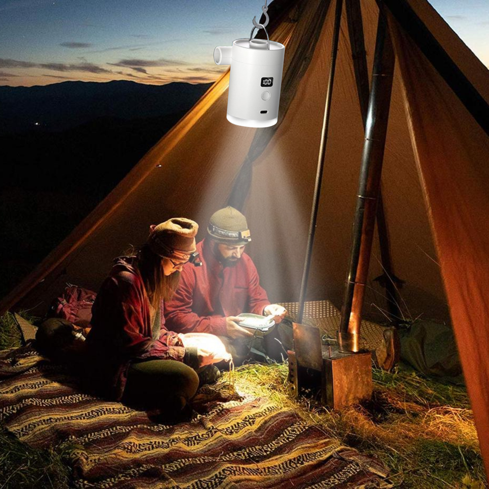 Zwei Personen lesen im Zelt unter Licht eines weißen Geräts. Nacht, Berge im Hintergrund.